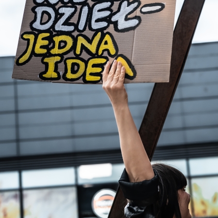 Osoba trzymająca transparent z napisem „Wiele dzieł, jedna idea” podczas wydarzenia