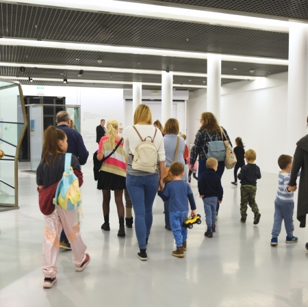 group of adults and children in exhibition space listening to education