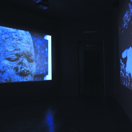 Sala wystawiennicza z wyświetlonymi filmami na ścianach