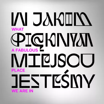 Na szarym tle napis ze stylizowanych liter w kolorze czarnym "W jakim pięknym miejscu jesteśmy", pod każdym słowem tłumaczenie w języku angielskim: What a Fabulous Place We Are in