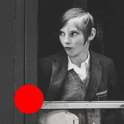 Na czarno-białym zdjęciu znajduje się dziewczynka z krótkimi włosami. Spogląda ona w prawą stronę. Na lewym, dolnym rogu znajduje się duża, pomarańczowa kropka. 