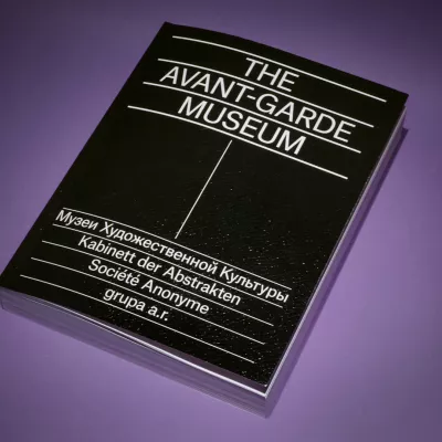 Na fioletowym tle leży książką. Książką ma czarną okładkę i napisy: AVANT-GARDE THE MUSEUM  der Abstrakten grupa Anonyme a.r.”