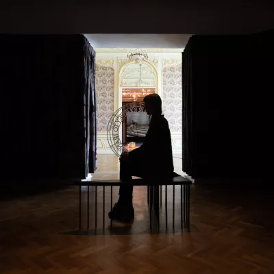 A woman is sitting in a dark room. In the background, there is light. 