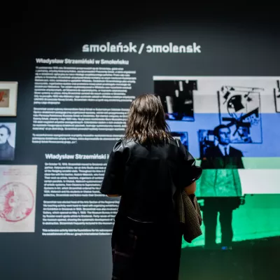 Przestrzeń wystawy "Awangardowe muzeum". Na tle ściany z informacjami dotyczącymi hasła "Smoleńsk" tyłem do widza stoi kobieta. 