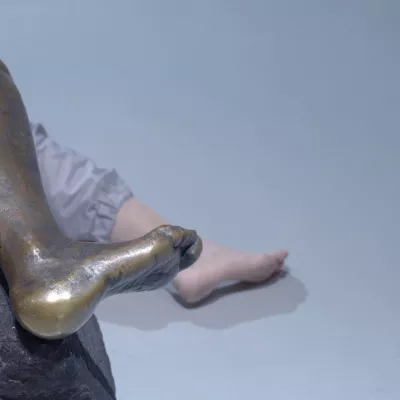 The photo shows Agata Siniarska, the artist. She is lying on the floor, only her leg is in the frame. There is a sculpture above the artist; only the leg of the sculpture is in the frame. The artist imitates the pose of a sculpture.