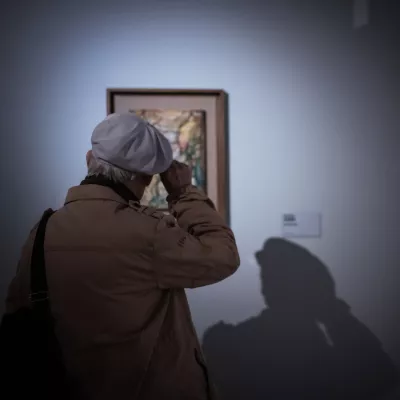 Starsza osoba patrzy na niewielki obraz wiszący na białej ścianie