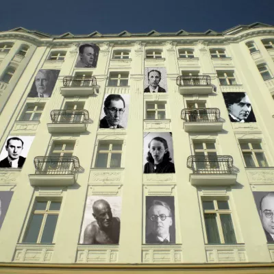 fotmontaż, widoczna z dołu wysoka kamienica, w niektrych jej oknach znajdują się wizerunki kobiet i mężczyzn