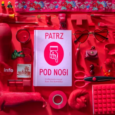 Zdjęcie przedstawia symetryczną kompozycję typu knolling, w której centralnym punktem jest książka pt. „PATRZ POD NOGI” autorstwa Kory Tei Kowalskiej, otoczona mnóstwem drobnych przedmiotów. Wszystkie elementy – w tym okulary w kształcie serc, papryczka chili, nożyczki, klocki LEGO czy taśma klejąca – oraz samo tło mają intensywny, czerwony kolor, co tworzy niemal jednolity, monochromatyczny kolaż.