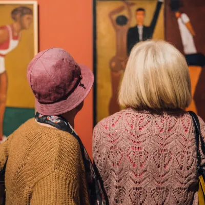 Dwie starsze kobiety, widziane od tyłu, stoją przed obrazami w muzeum sztuki. 