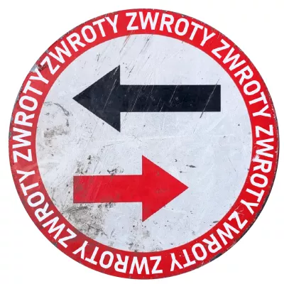 Okrągły znak drogowy. Tło znaku jest białe, a po jego obwodzie biegnie czerwony okrąg. Wewnątrz tego okręgu, na białym tle, umieszczone są dwie poziome strzałki. Górna strzałka jest czarna i skierowana w lewo, natomiast dolna strzałka jest czerwona i skierowana w prawo.  Wzdłuż czerwonego obwodu znaku, białymi literami, powtarza się słowo "ZWROTY".
