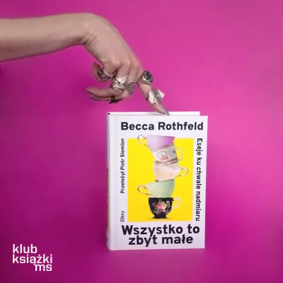 Zdjęcie przedstawia białą książkę trzymaną przez prawą rękę, na palcach której widać wiele srebrnych pierścionków. Książka ma na okładce tytuł "Wszystko to zbyt małe" (oryg. "Eseje ku chwale nadmiaru") oraz wieżę z pięciu filiżanek na żółtym tle. Całość jest na intensywnie różowym tle. W lewym dolnym rogu znajduje się logo "klub książki ms".